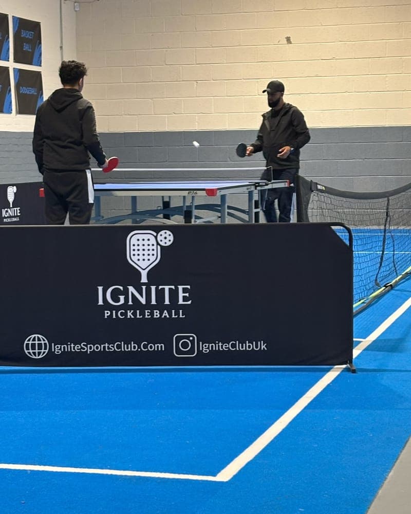 Two players at a table tennis table behind a black Ignite court banner